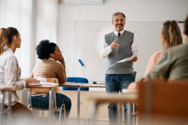 Happy mature professor giving lecture to adult students in the classroom.